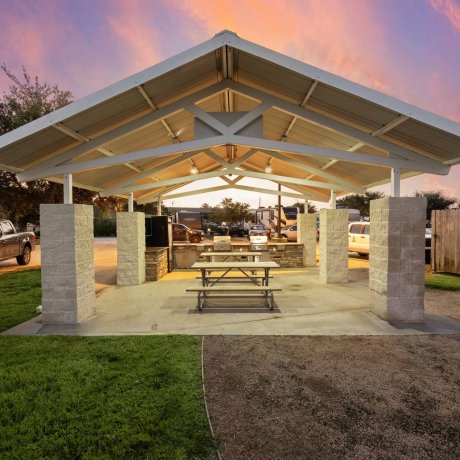 Covered BBQ pavilion with picnic tables at Westlake RV Resort in Houston, TX at twilight