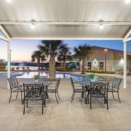 Covered poolside seating with ornate metal tables and chairs overlooking Highway 6 RV Resort pool at twilight — Houston, TX pet-friendly monthly stays
