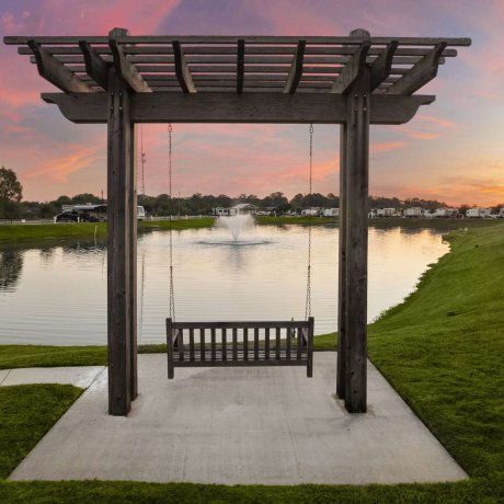 Wooden swing overlooking the lake and fountain at Fallbrook RV Resort in Houston, TX during sunset.