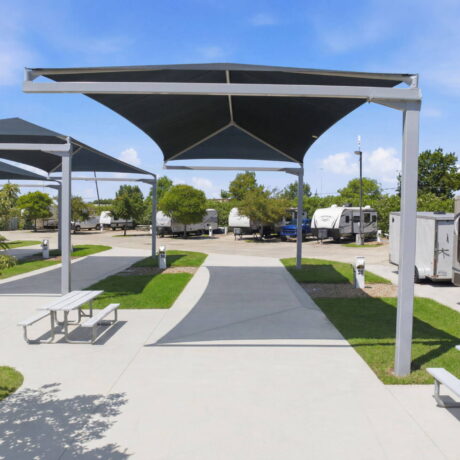 Ground-level view of premium covered RV sites with concrete pads, shade canopies, aluminum picnic tables, and utility hookups at a luxury RV resort.