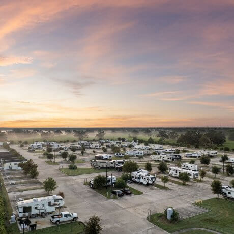 Lower aerial view of full hookup RV sites at Brazoria Lakes RV Resort during sunrise, with morning mist, pasture, and trees in Brazoria, Texas