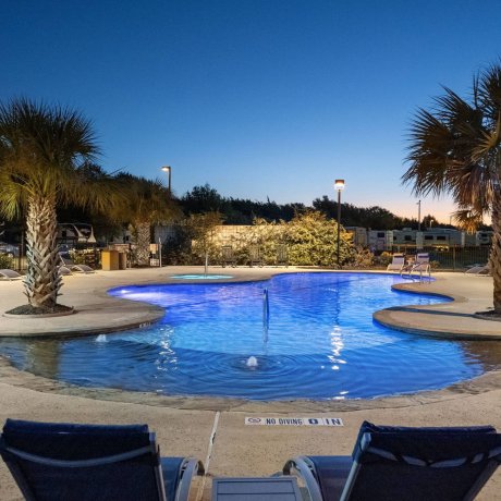 Highway 6 RV Resort illuminated pool at dusk with palm trees, lounge chairs, and spa area — Houston, TX pet-friendly monthly stays