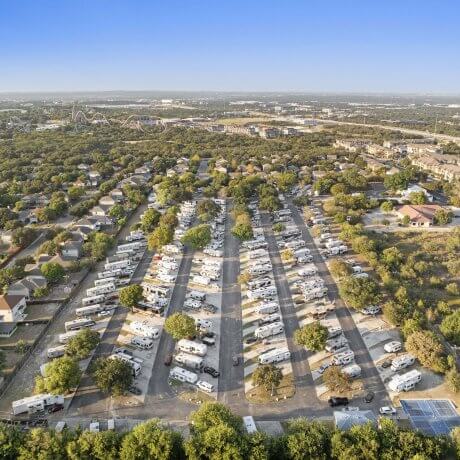 High-resolution aerial photo of Admiralty RV Park in San Antonio, Texas, showing full RV site layout surrounded by residential homes, trees, and nearby theme park attractions.