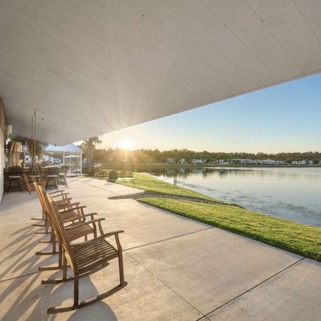 Rocking chairs behind clubhouse at Eastlake RV Resort in Houston, TX overlooking lake and fountain at sunrise with BBQ area in background near 77044
