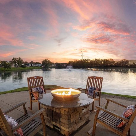 Fire pit surrounded by wooden chairs with lake view at Southlake RV Resort in Houston